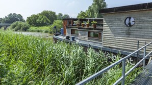 Een woonboot met een dek, plantenbakken en een raam.