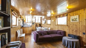 Een gezellig interieur van een blokhut met houten plafond, een bank, een eettafel en een keukenhoek.