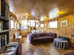 A cozy cabin interior with wooden walls, a sofa, a dining table, and a kitchen area. - Boat Getaway Near Lake (Houthulst)