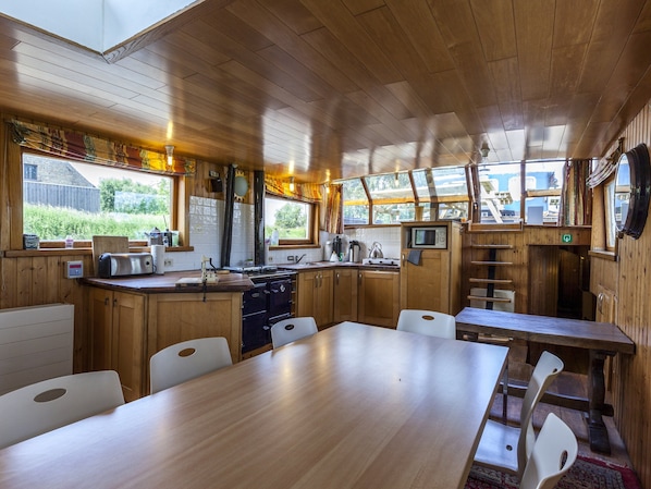 A cabin-style kitchen with wooden cabinets, a stove, a microwave, and a dining area with a table and chairs.
