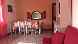 A dining area with a table set for four, a red sofa, and a mirror above the table. - Apartment in Santa Teresa Near the Beach (Santa Teresa di Gallura)