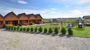 En række træhytter med en legeplads og picnicområde foran.