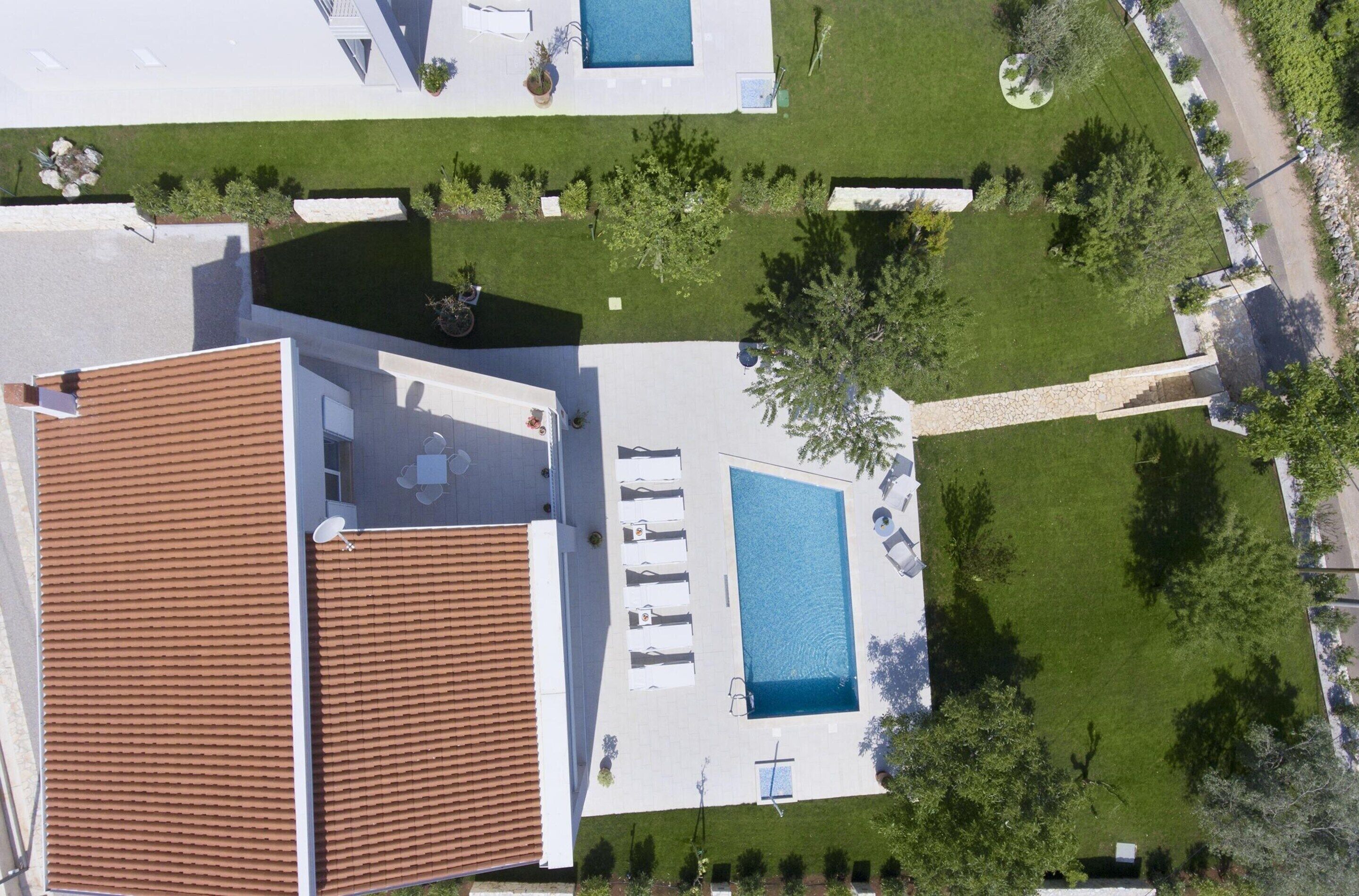 Vista aèria d'una propietat residencial amb piscina, terrassa coberta i jardí ben cuidat.