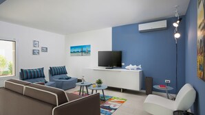 A modern living room with a sofa, a white chair, a small table, and a TV on a white cabinet. - Exquisite Villa in Stanisovi With Swimming Pool (Rasa)