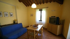 Un accogliente soggiorno con un divano blu, un tavolo da pranzo in legno e sedie. C'è una televisione su un mobile in legno e una finestra con tende.