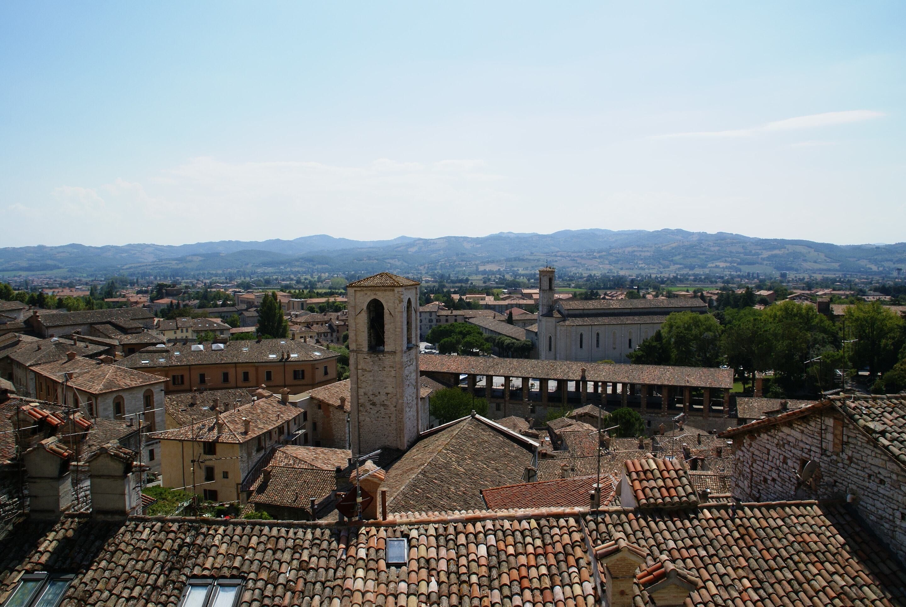 A historic town with terracotta-tiled roofs, a prominent church tower, and a backdrop of rolling hills.