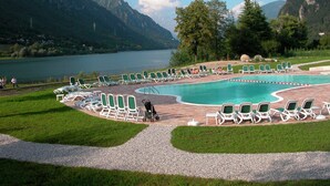 A pool area with lounge chairs and a person pushing a stroller, surrounded by mountains and a lake. - Apartment in Idro With Lake and Mountain Views (Idro)