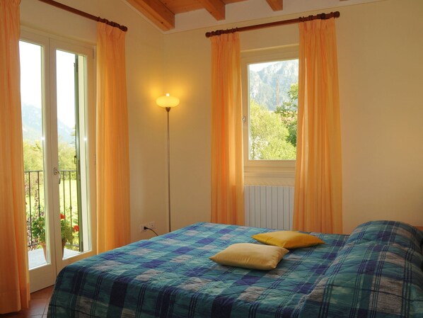 A bedroom with a bed, two pillows, a floor lamp, and a window with curtains.