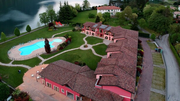 A large building with a swimming pool, surrounded by lush greenery and a lake. - Apartment in Idro With Lake and Mountain Views (Idro)