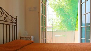 Un dormitorio con cama, ventana y vista a la vegetación exterior.