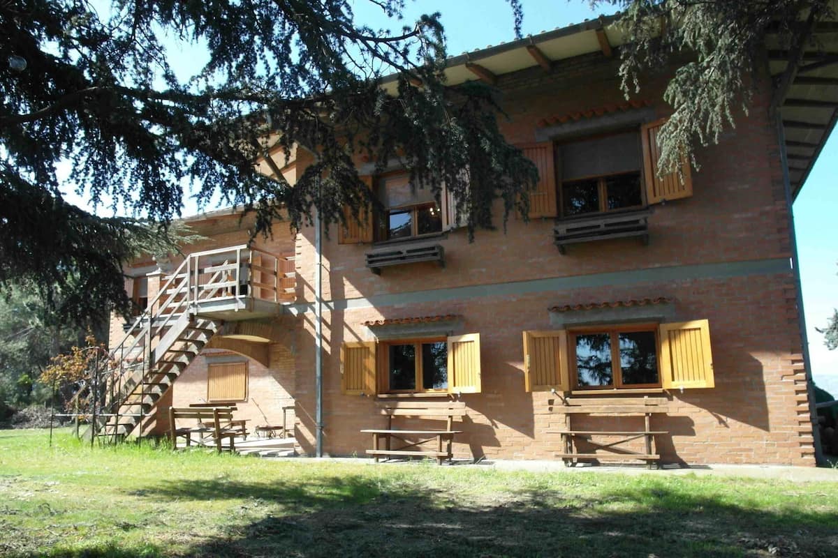 A two-story brick building with wooden shutters, a staircase, and picnic tables.