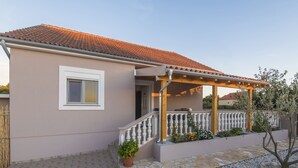 A two-story house with a tiled roof, a covered porch with a railing, and a small garden area with a potted plant. - Holiday Home Near Zadar With Private Pool (Posedarje)