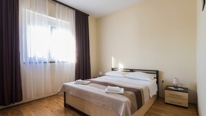 A neatly made bed with a white and brown striped bedspread, a bedside table with a lamp, and a large window with sheer curtains. - Holiday Home Near Zadar With Private Pool (Posedarje)