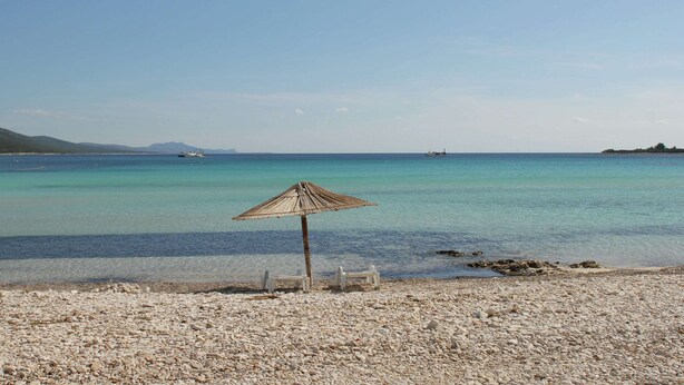 A pebbled beach with a wooden umbrella and two white chairs. - Holiday Home in Veli Rat Near Saharun (Sali)