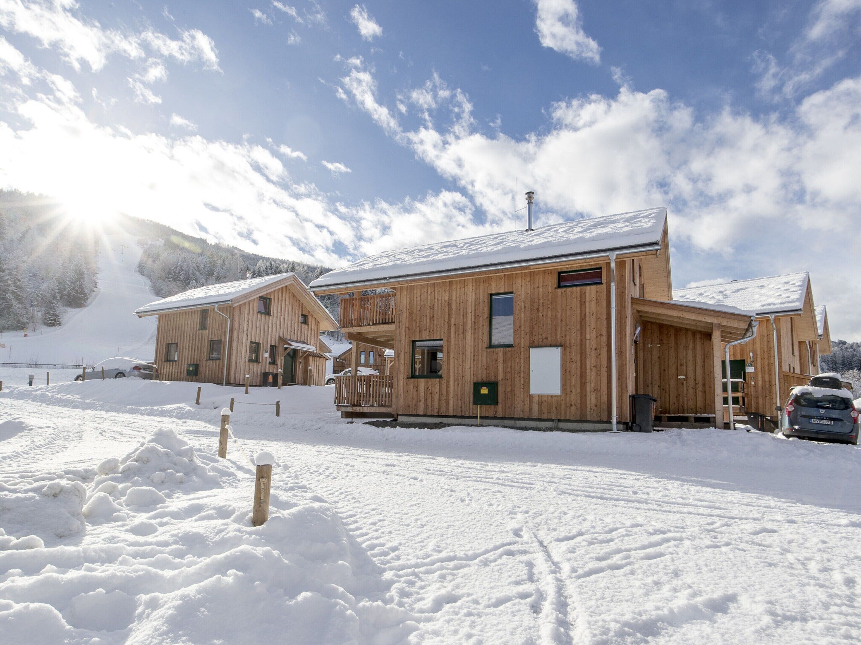A wooden cabin with a balcony, surrounded by snow-covered ground and a clear sky.
