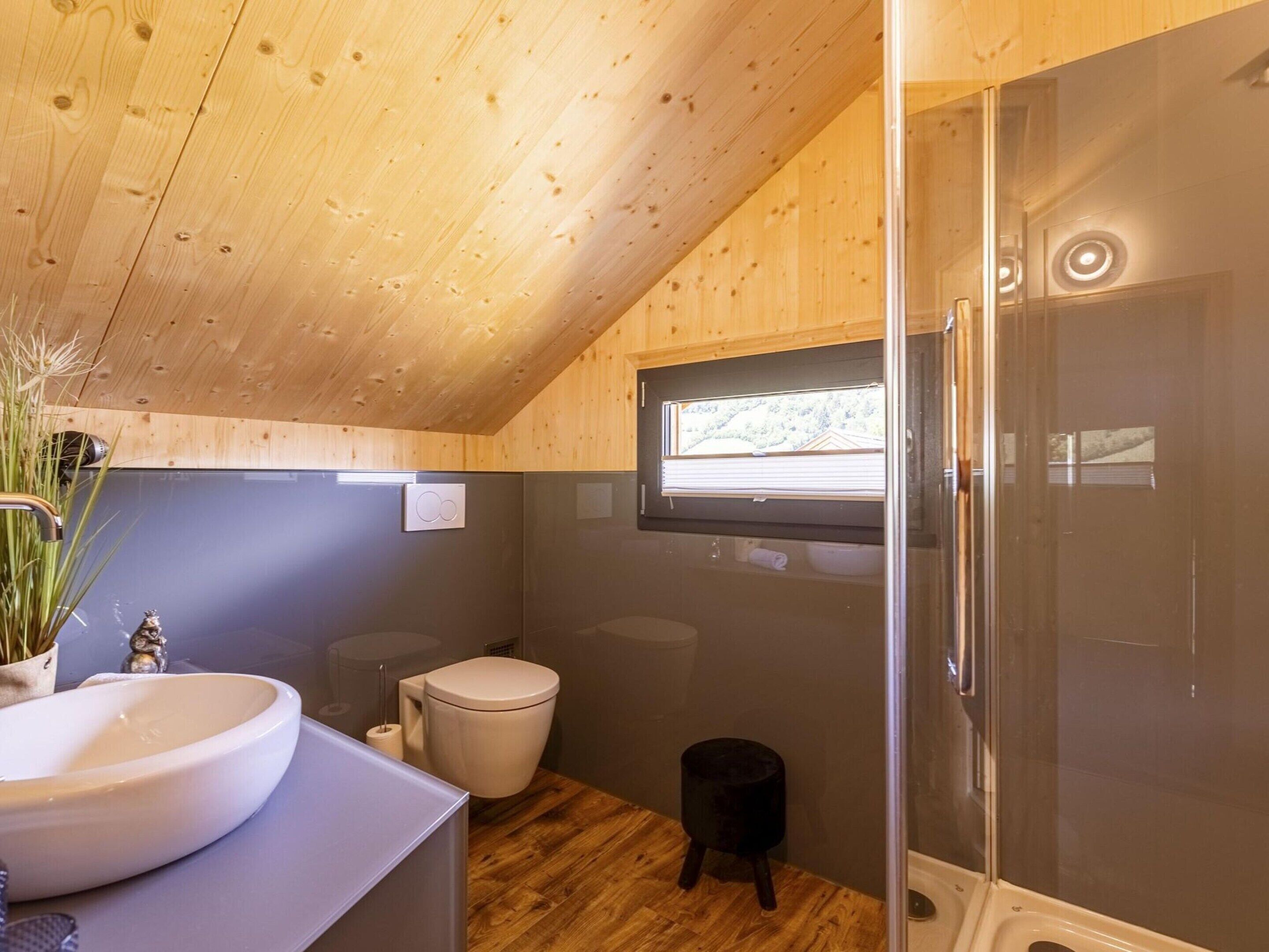 Un baño pequeño con techo de madera, un lavamanos amplio, un inodoro y un box de ducha de vidrio.