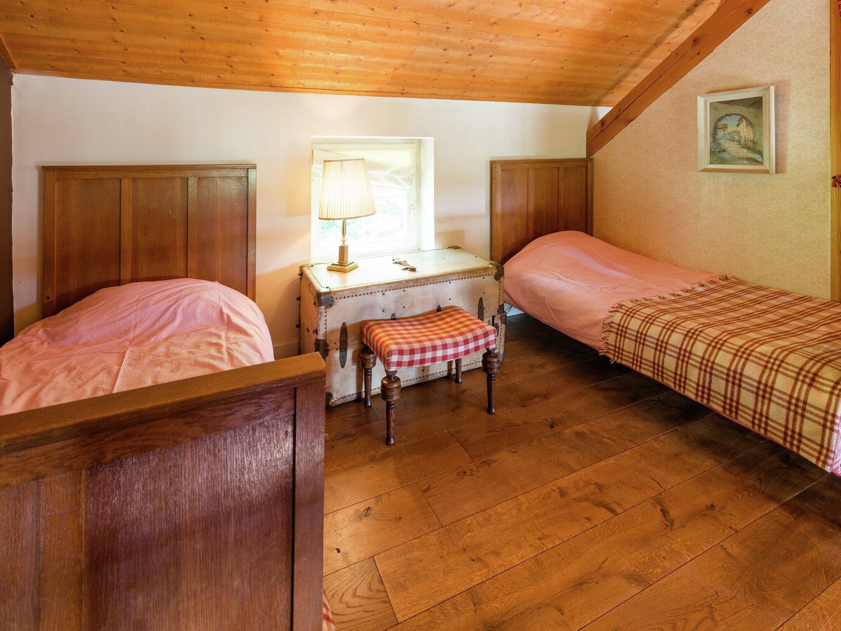 Een gezellige kamer met twee houten bedden, een klein bureau met een lamp en een raam.