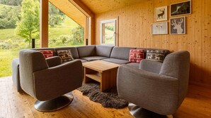 Un salon moderne doté d’un grand canapé d’angle, d’une table basse en bois et offrant une vue sur un paysage verdoyant grâce à de grandes fenêtres.