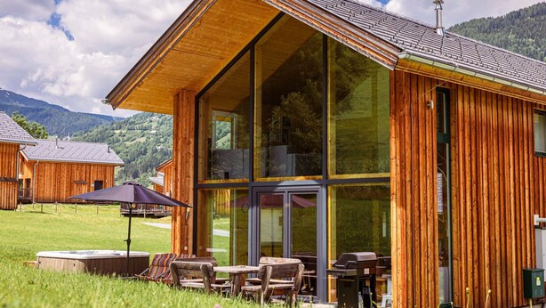 Une cabane en bois dotée de grandes fenêtres et d’un espace patio avec des sièges d’extérieur.