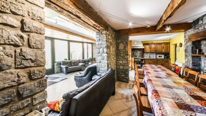 A spacious living area with a stone wall, leather sofas, a dining table with chairs, and a kitchen in the background. - Stone Cottage with Sauna & Hot Tub near Cave of Lorette in Rochefort (Rochefort)