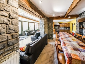A spacious living area with a stone wall, leather sofas, a dining table with chairs, and a kitchen in the background. - Stone Cottage with Sauna & Hot Tub near Cave of Lorette in Rochefort (Rochefort)