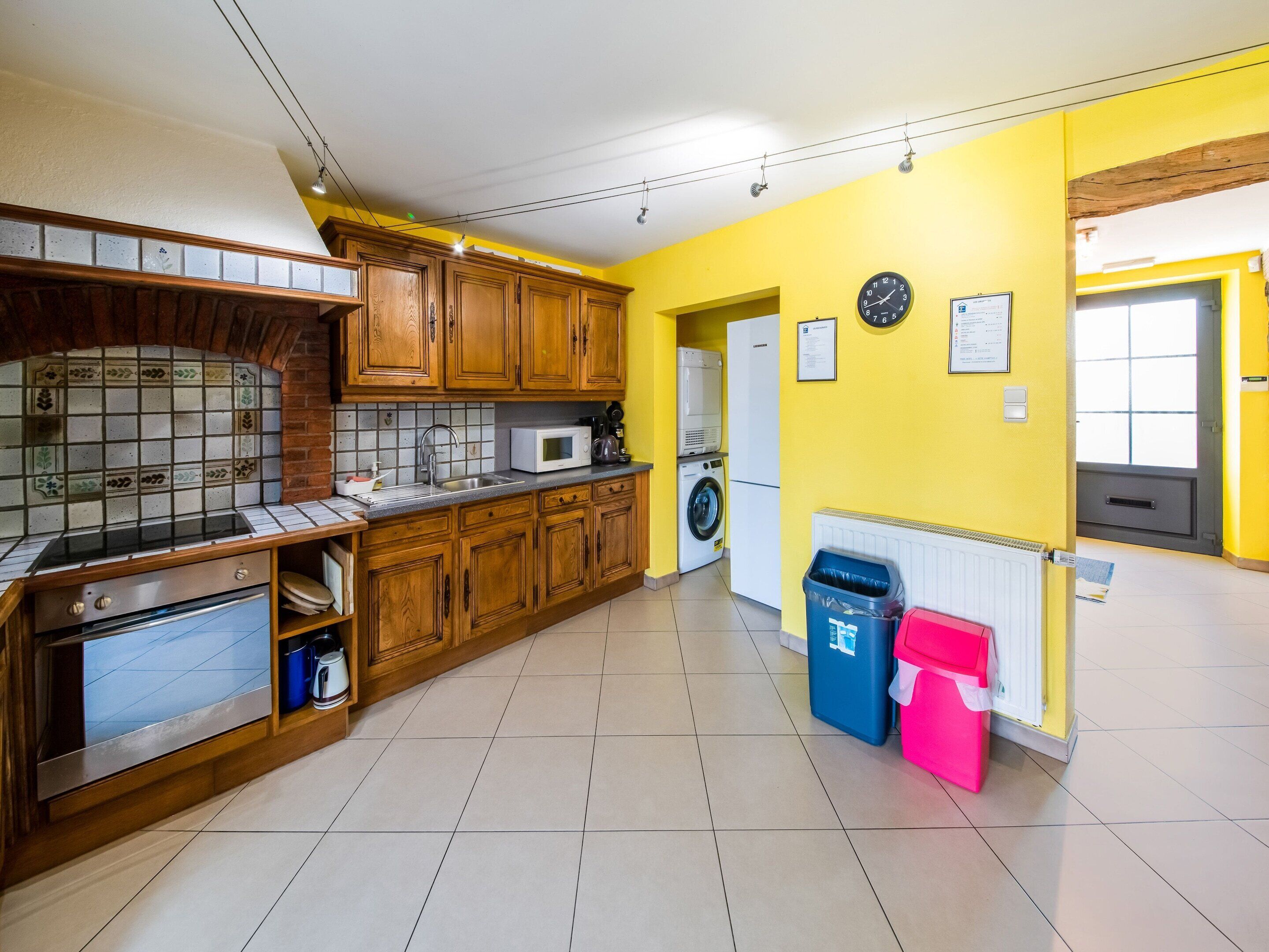 A kitchen with wooden cabinets, a microwave, a washing machine, and a trash bin.