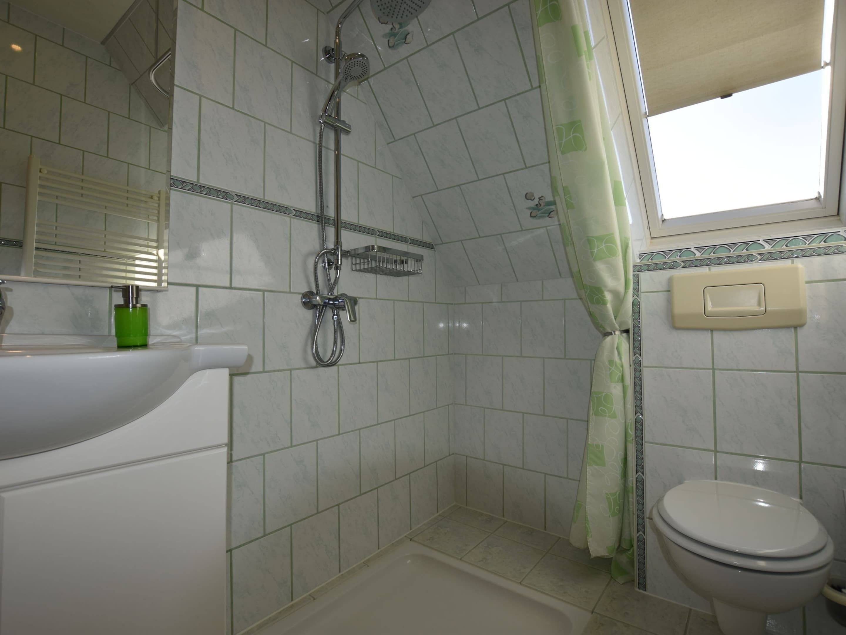 A bathroom with a shower, toilet, sink, and a window with a curtain.