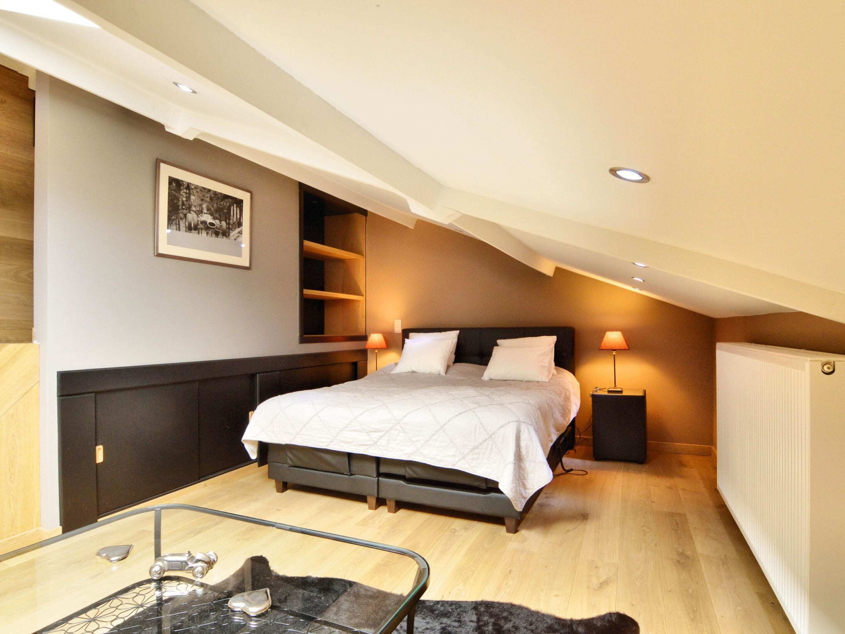 Une chambre à coucher avec un lit, des lampes de chevet, une table en verre avec une chaise et un radiateur.
