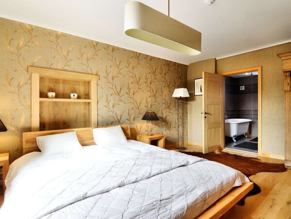 A bedroom with a large bed, wooden headboard, a bedside table with a lamp, a wardrobe, and a bathroom visible through an open door. - Walk Luxury Stay With Pool (Waimes)