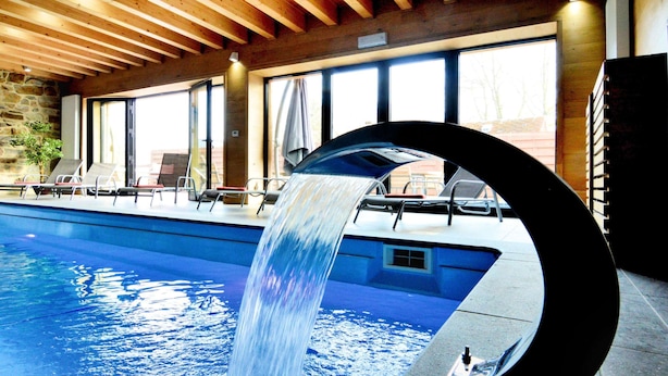 En swimmingpool med et vandfald, liggestole og store vinduer.
