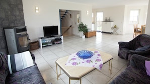 A living room with a fireplace, television, sofa, and a dining area with a table and chairs. - Ferienhaus in Hessen mit Grossem Garten (Voehl)