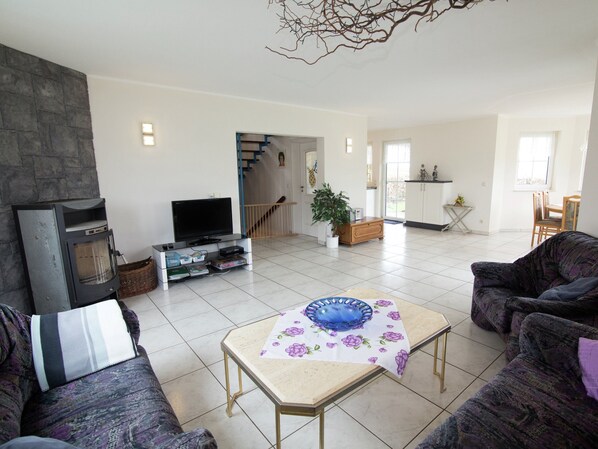 Ein Wohnzimmer mit Kamin, Fernseher, Sofa und einem Essbereich mit Tisch und Stühlen.