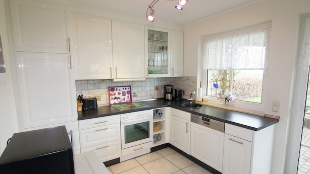 A kitchen with white cabinets, a black countertop, a coffee maker, and a window with a view. - Ferienhaus in Hessen mit Grossem Garten (Voehl)