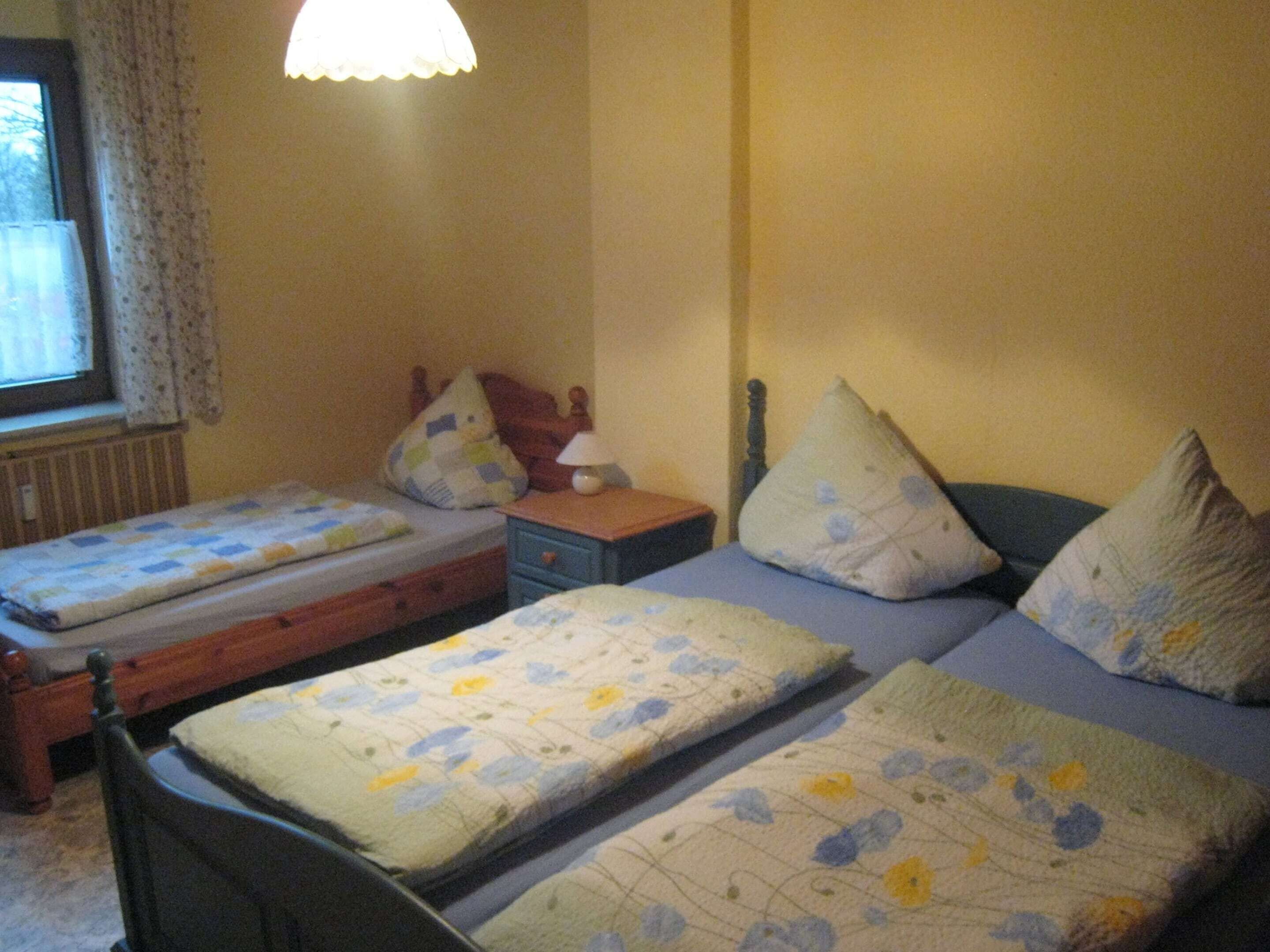 Een slaapkamer met twee eenpersoonsbedden, een nachtkastje, een lamp en een raam met gordijnen.