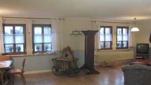A room with wooden flooring, a dining table with chairs, a television, and a large window with curtains. - Cozy Morbach Getaway (Morbach)
