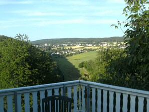 A view from a balcony overlooking a valley with houses and greenery.