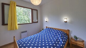 A bedroom with a bed, a window with curtains, a wall-mounted heater, and two wall sconces. - Holiday Home in Quillan Near Pyrenees (Quillan)