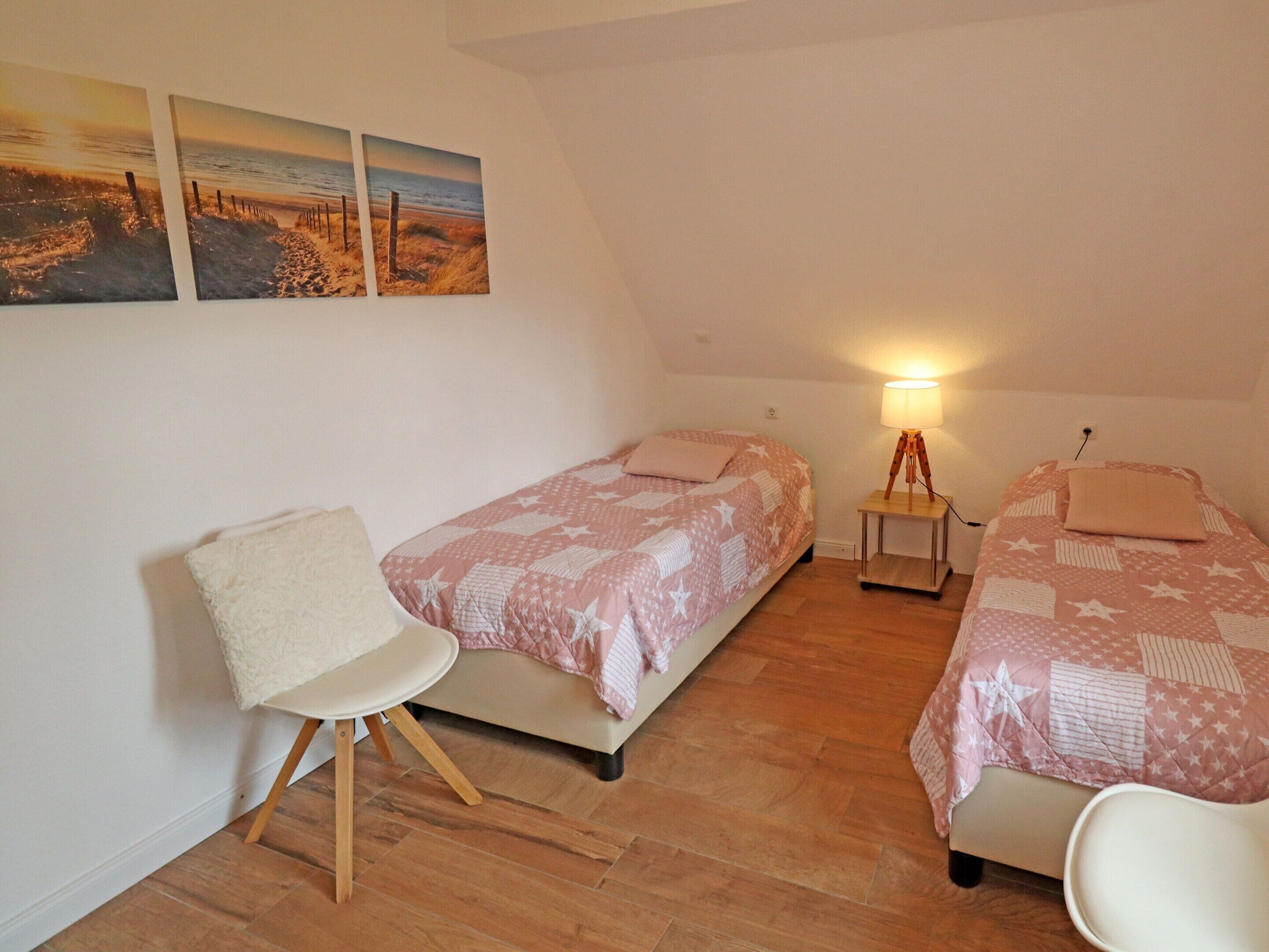 A small, cozy room with two beds, a chair, and a lamp.