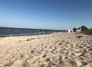 Une plage de sable avec des vagues, un ciel dégagé et quelques personnes au loin.