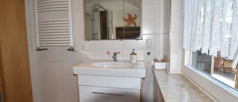 Un baño con lavamanos blanco, espejo y suelo de madera.