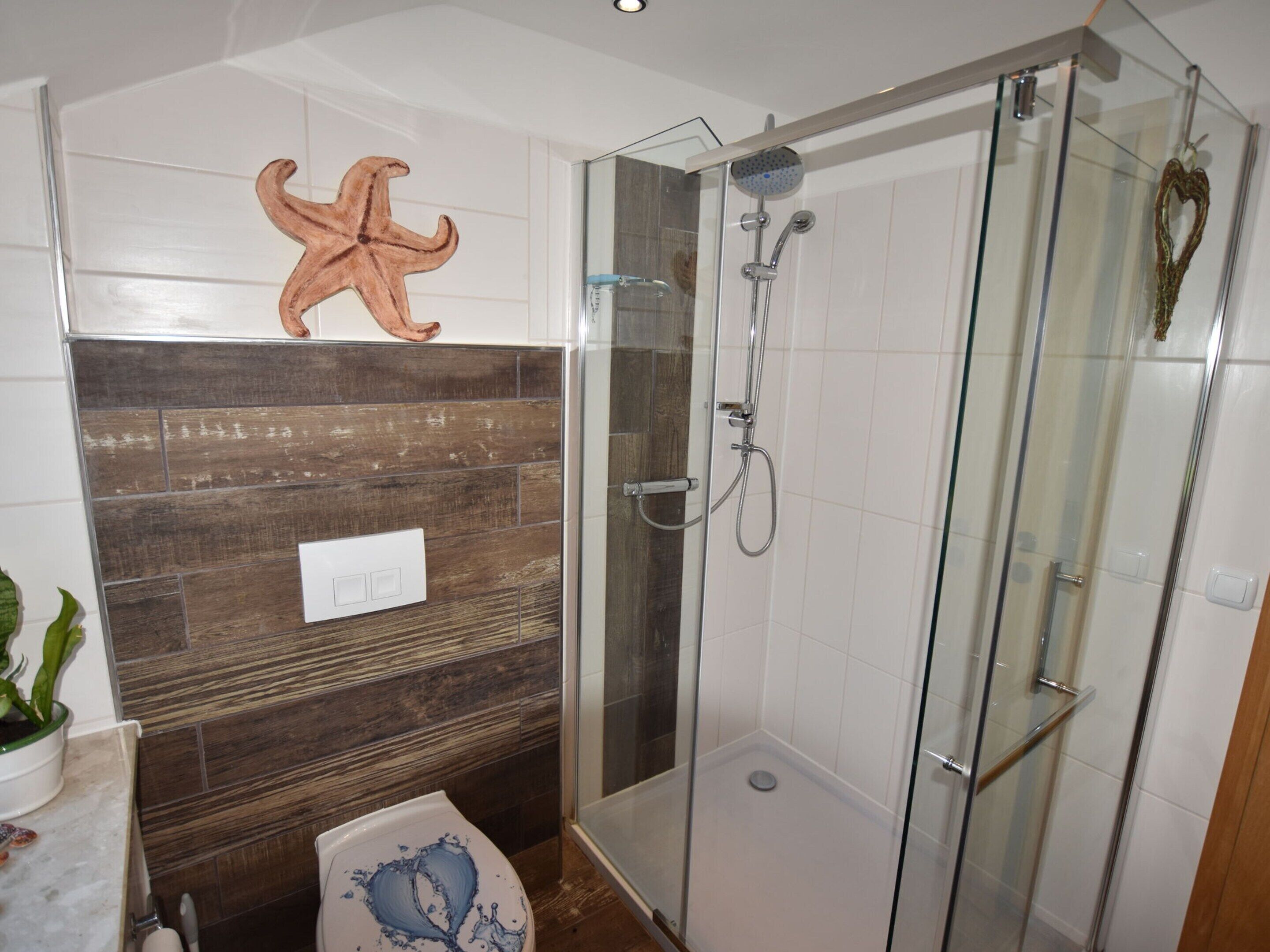 Un baño moderno con cabina de ducha de vidrio, una pared de acento de madera y una estrella de mar decorativa.