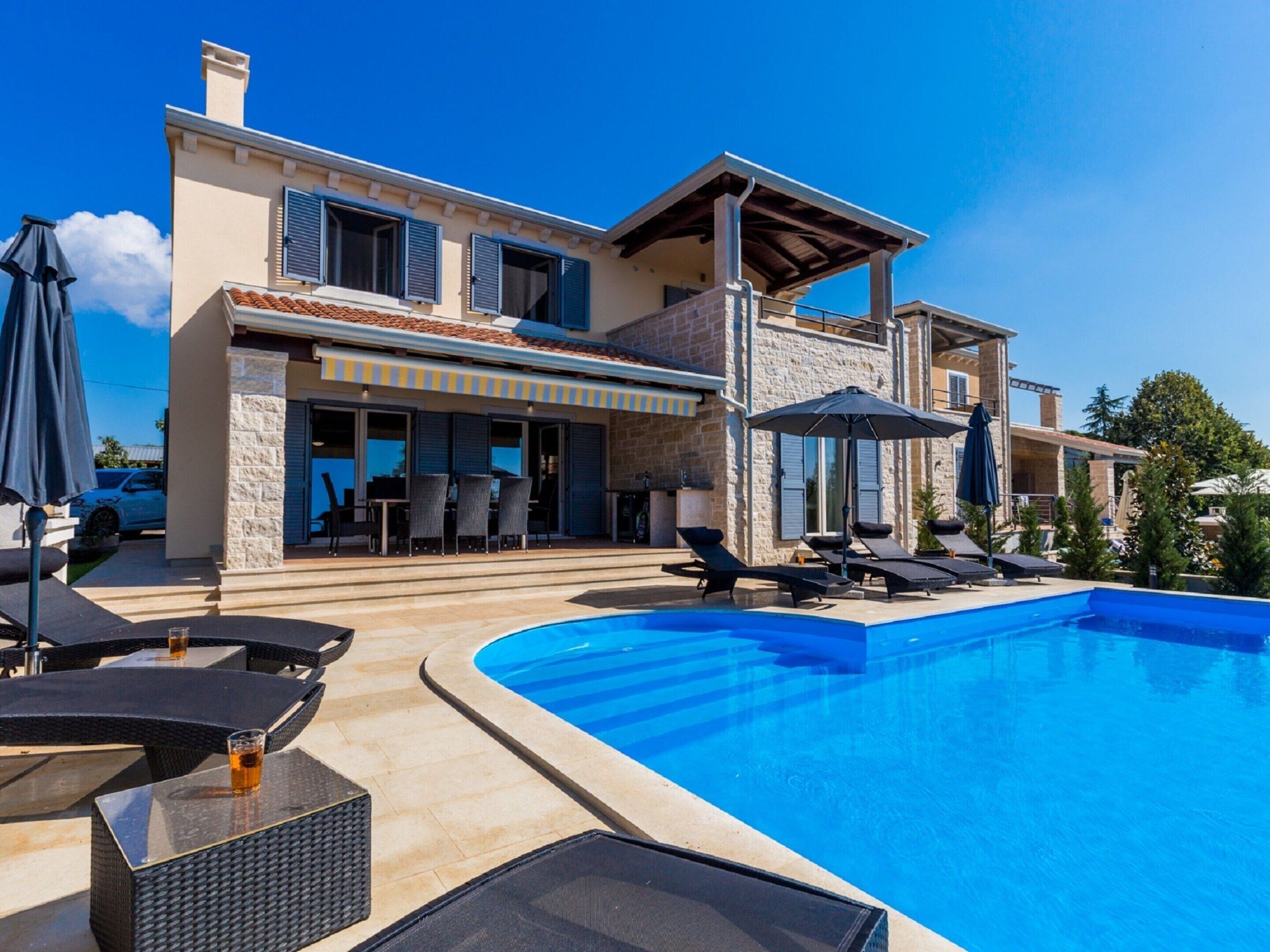 A modern villa with a swimming pool, outdoor seating, and a covered patio.