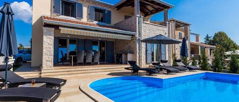 A modern villa with a swimming pool, outdoor seating, and a covered patio.