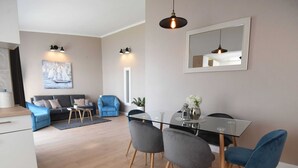 Una sala de estar moderna con una mesa de comedor de vidrio, sillas grises y azules, un sofá y un cuadro en la pared.