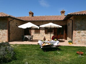 A stone building with a tiled roof, two outdoor umbrellas, a table with food, and a grassy area. - Farmhouse Near Lake Trasimeno With Pool (Passignano sul Trasimeno)