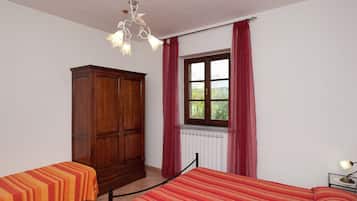Quarto com cama, guarda-roupa, janela com cortinas e radiador.