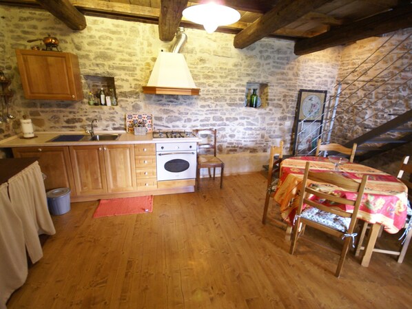 Une cuisine rustique avec un mur en pierre, des armoires en bois, une cuisinière à gaz et un coin repas comprenant une table et des chaises.