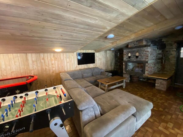 A cozy indoor space with a foosball table, a sofa, a television, and a stone fireplace.