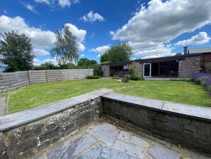 A stone retaining wall, a grassy lawn, and a modern brick building with large windows and a chimney. - Spacious Waimes Villa (Waimes)