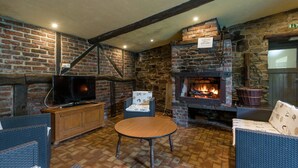 A cozy room with a stone fireplace, a television, wicker furniture, and a tiled floor. - Spacious Waimes Villa (Waimes)